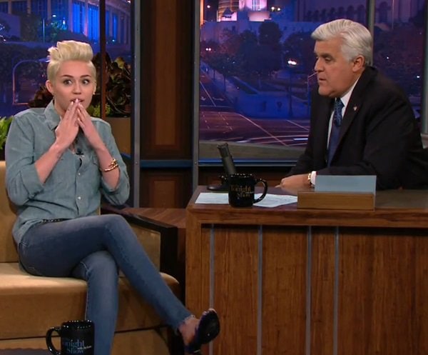 Miley Cyrus chats with Jay Leno on The Tonight Show in Los Angeles on January 30, 2014, wearing a chambray Saint Laurent shirt, skinny jeans, and ankle-strap sandals
