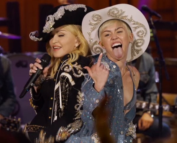 Miley Cyrus rocks a bedazzled denim ensemble and a white embellished cowboy hat while performing with Madonna at MTV Unplugged, flashing her signature tongue-out pose