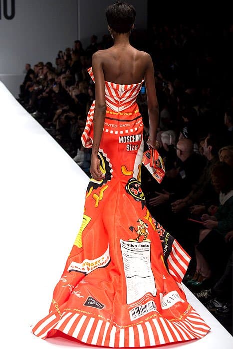 This full-length rear view of a Moschino Fall 2014 runway look displays a model wearing a strapless gown designed to resemble snack food packaging
