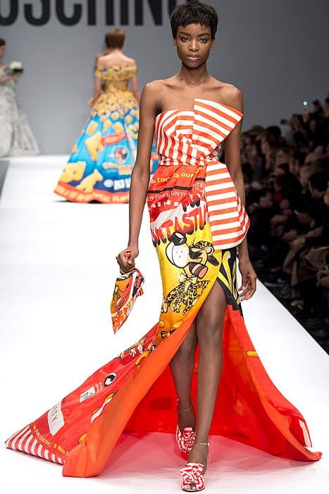 Moschino Fall 2014 showcases a chic, strapless gown inspired by snack food packaging, featuring a bold mix of red stripes, yellow, and red graphics, a high split, and a dramatic train, paired with red and white printed heels