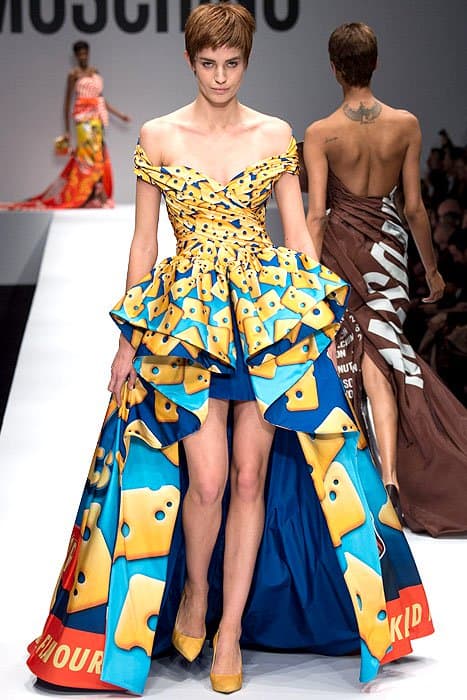 Moschino Fall 2014 presents a playful 'cheese crackers' dress, featuring an off-the-shoulder neckline, a short front, and a dramatic high-low skirt with a vibrant blue and yellow pattern, paired with yellow heels