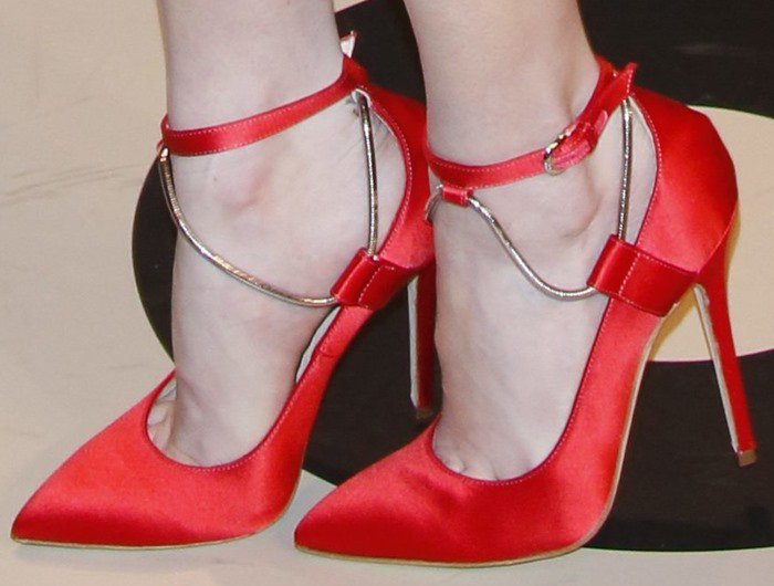 The red satin Brian Atwood “Kaela” pumps feature slender ankle straps with delicate chain detailing, adding a subtle edge to the otherwise classic pointed-toe silhouette