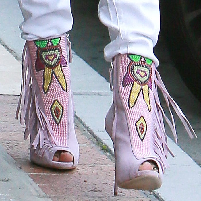 Jennifer Lopez's blush-pink Giuseppe Zanotti peep-toe booties combine suede fringe with intricate beadwork inspired by Southwestern and Mayan geometric motifs, transforming an otherwise monochrome outfit into a statement look