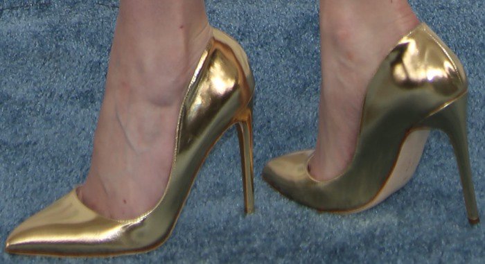 Krysten Ritter showcases her gold Rupert Sanderson “Elba” pumps, a metallic finish that perfectly complements her statement Versace dress