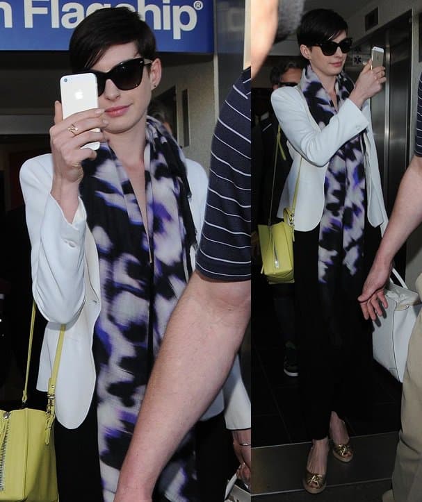 Anne Hathaway playfully turns the tables on photographers at LAX, styling a white blazer, oversized printed scarf, citron yellow Balenciaga Mini Papier A4 bag, and metallic espadrilles for a polished yet personality-driven airport look on March 10, 2014