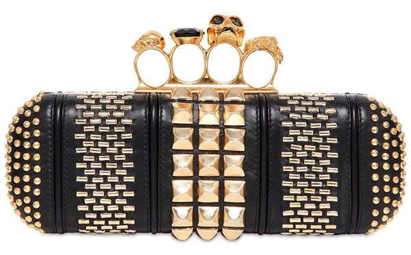 A studded black leather Alexander McQueen knuckle box clutch featuring gold-tone hardware, skull-topped rings, and bold geometric embellishments