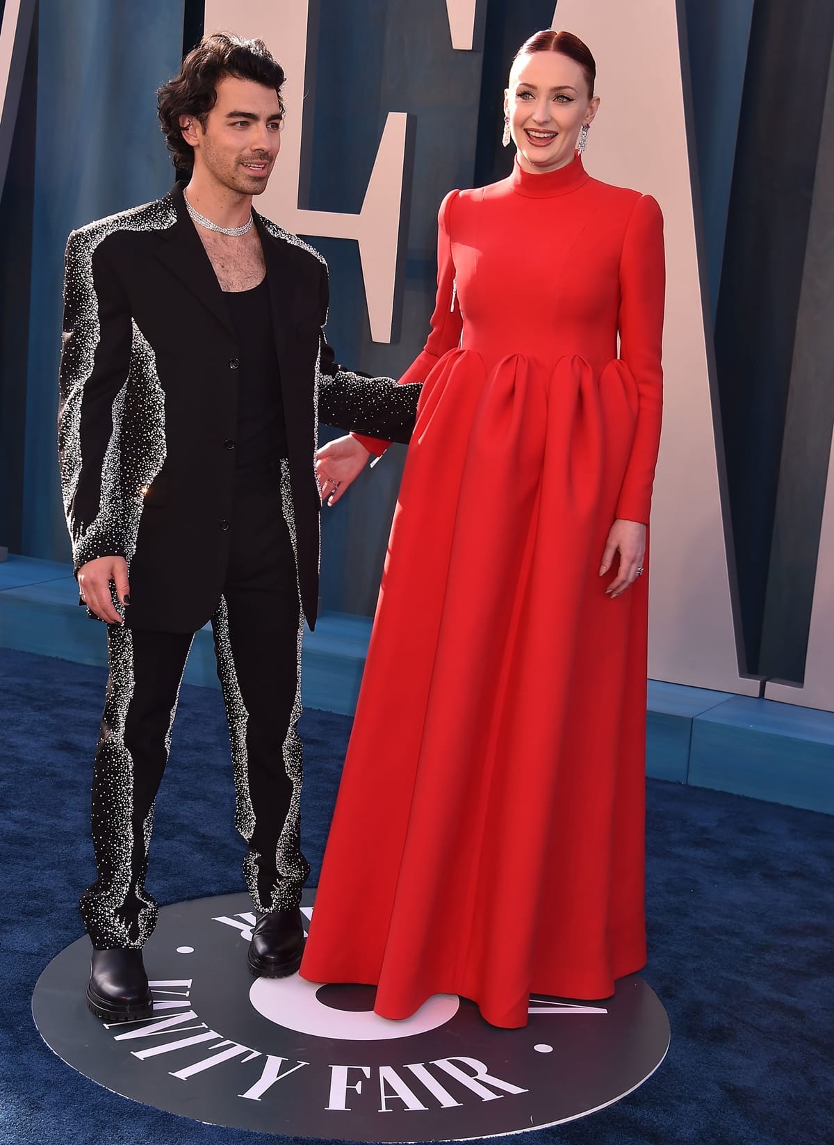 Sophie Turner wears a red Louis Vuitton dress and metallic gold sandals alongside Joe Jonas at the 2022 Vanity Fair Oscar Party