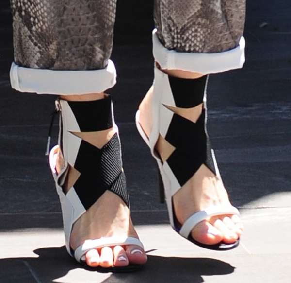 A close-up of Gwen Stefani's stylish L.A.M.B. "Reina" sandals featuring monochrome elastic crossover straps and snake-embossed trims, perfectly complementing her chic outfit