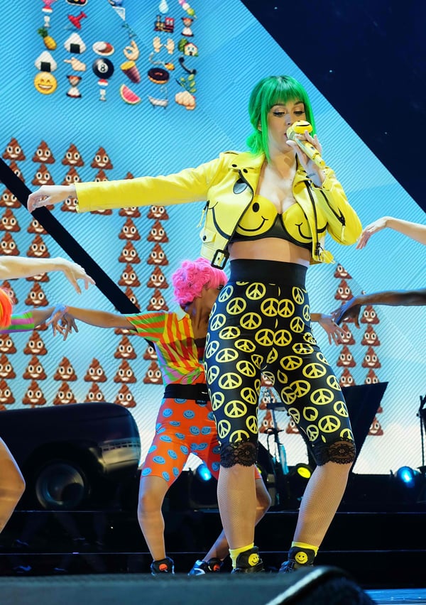 Katy Perry performs on stage in a Moschino smiley ensemble with green hair during her Prismatic World Tour, highlighting her quirky fashion sense