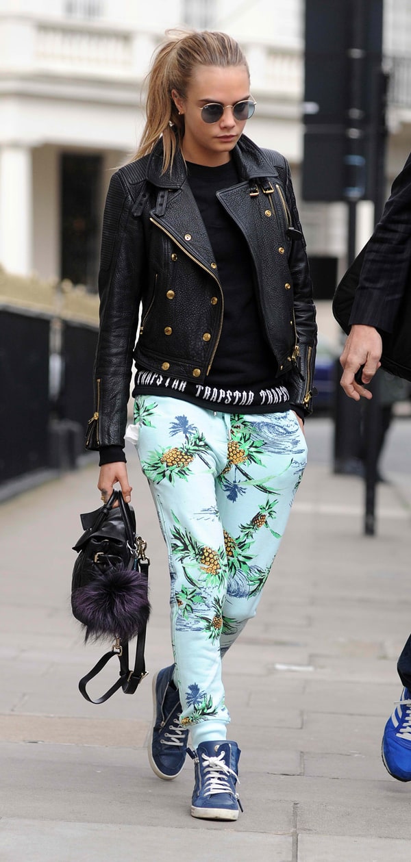 Cara Delevingne adds an edgy touch to her look with a black leather jacket and tropical print drawstring pants, paired with blue high-top sneakers for a stylish streetwear vibe