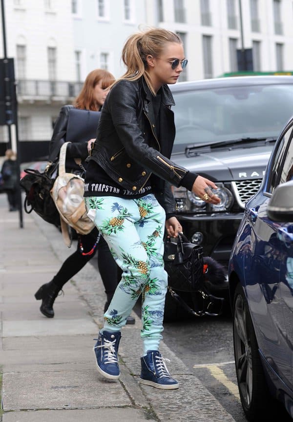 Cara Delevingne adds edge to tropical drawstring pants by pairing them with a black leather jacket and blue high-top sneakers