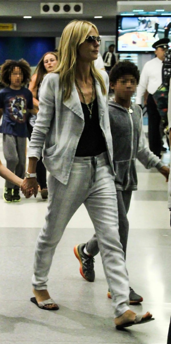 Heidi Klum showcases a chic travel look with a light gray blazer and matching drawstring pants, paired effortlessly with a black top and stylish sandals