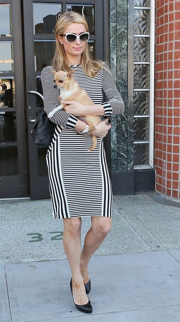 Paris Hilton styled a striped body-con dress with black Alaïa pumps, a quilted Chanel shoulder bag, and retro-inspired white sunglasses