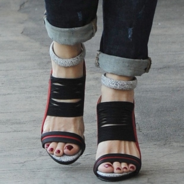 Gwen Stefani’s striking GX by Gwen Stefani ‘Haru’ sandals feature bold black straps, red accents, and printed ankle cuffs with a back zipper design, complemented by her flawless red pedicure that ties her entire look together