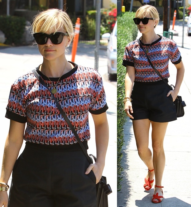 Reese Witherspoon pairs a vibrant, textured top with chic black shorts, finishing the look with bold red strappy heels for a playful yet polished summer vibe in Los Angeles