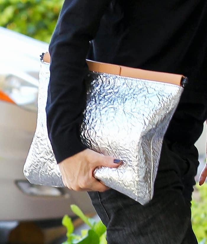 Gwen Stefani carries the L.A.M.B. Fallon silver and natural leather clutch, featuring a bold crinkled foil texture and sleek oversized silhouette