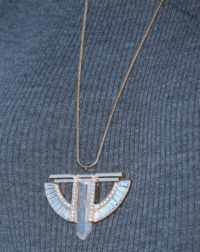 Her geometric pendant—set with baguette-cut stones and a translucent crystal drop—introduces an art-deco edge against the clean lines of her ribbed turtleneck dress