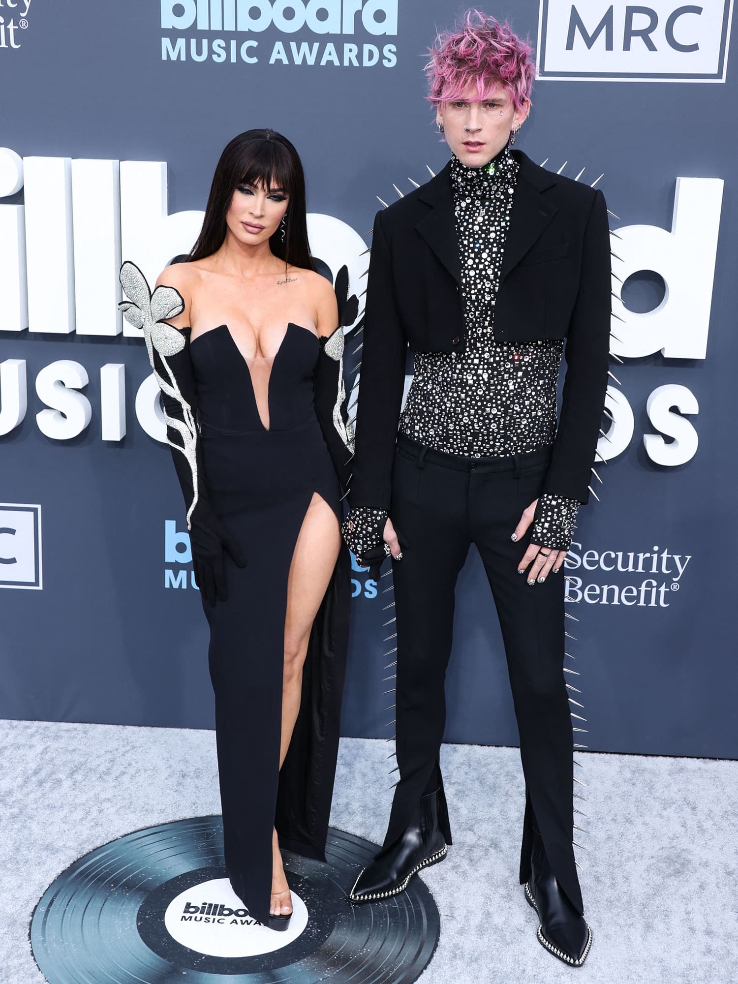 Megan Fox made a dramatic entrance alongside Machine Gun Kelly at the 2022 Billboard Music Awards in Las Vegas, grounding her Morticia-inspired black David Koma gown with towering platform heels that amplified the look’s gothic edge