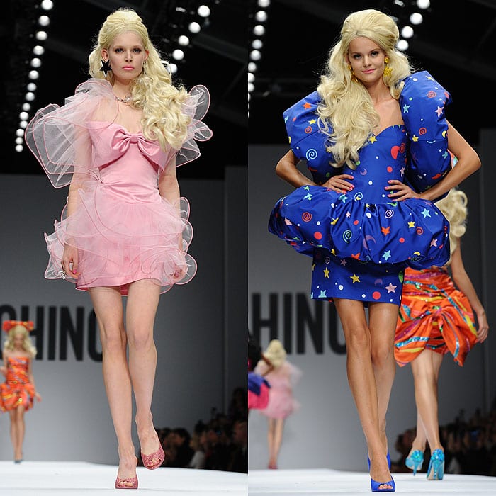 Two models display Barbie-inspired fashion from Moschino's Spring 2015 collection, one in a pink organza dress with a bow and the other in a bold blue dress adorned with colorful stars and bows