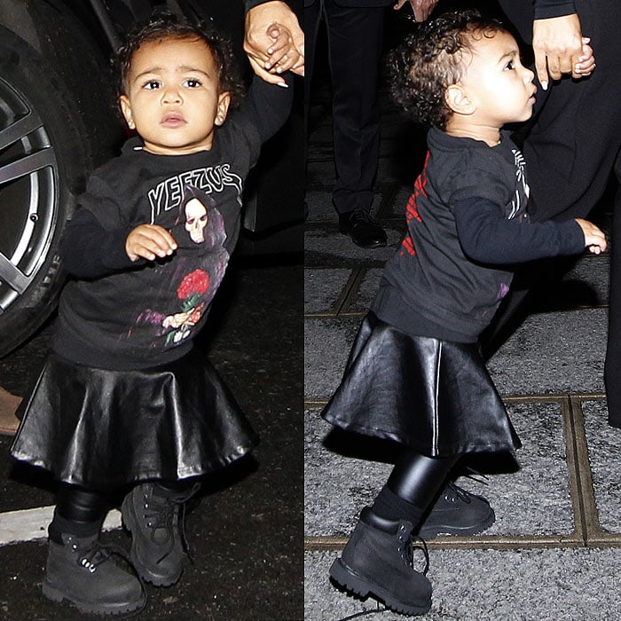 Baby North West toddles beside Kim Kardashian in a Yeezus tour sweatshirt, leather skirt, and chunky lace-up Timberland boots during Paris Fashion Week