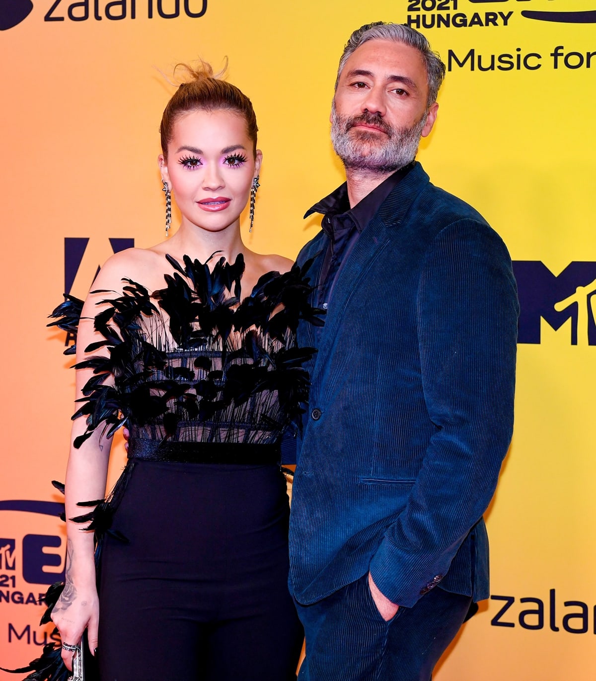 Rita Ora and Taika Waititi arrive at the 2021 MTV Europe Music Awards in Budapest, with Ora’s feathered Jean-Louis Sabaji look delivering high-impact glamour alongside her partner’s sharp tailoring