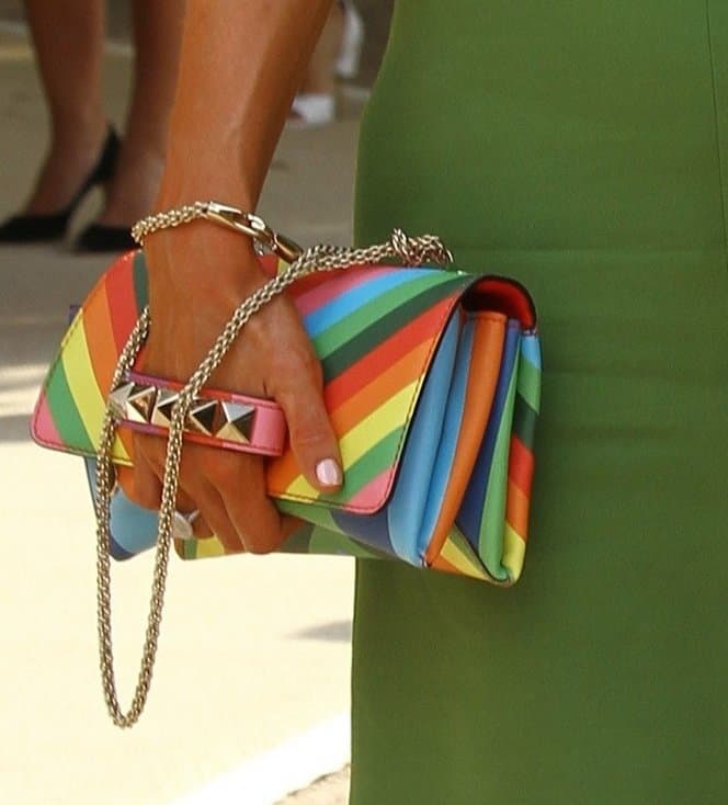 Paris Hilton adds a playful burst of color to her Valentino runway-show look with a rainbow-striped “Va Va Voom” studded clutch finished with the brand’s signature pyramid hardware and chain strap