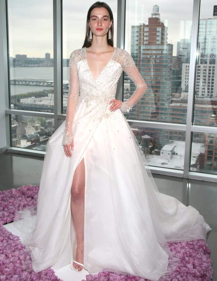 A sheer, crystal-embellished bodice and flowing tulle skirt give the romantic gown modern edge, finished with minimalist white ankle-strap heels that subtly highlight the dramatic slit
