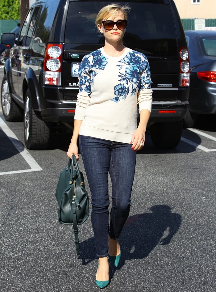 Reese Witherspoon masters effortless elegance by pairing a floral Tory Burch sweater with dark skinny jeans, emerald green Manolo Blahnik pumps, and a structured teal Lanvin handbag, creating a chic and cohesive color-coordinated look