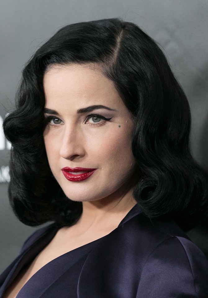 Dita Von Teese’s polished beauty look—defined by sculpted waves, winged eyeliner, and crimson lips—complements her vintage-inspired evening ensemble
