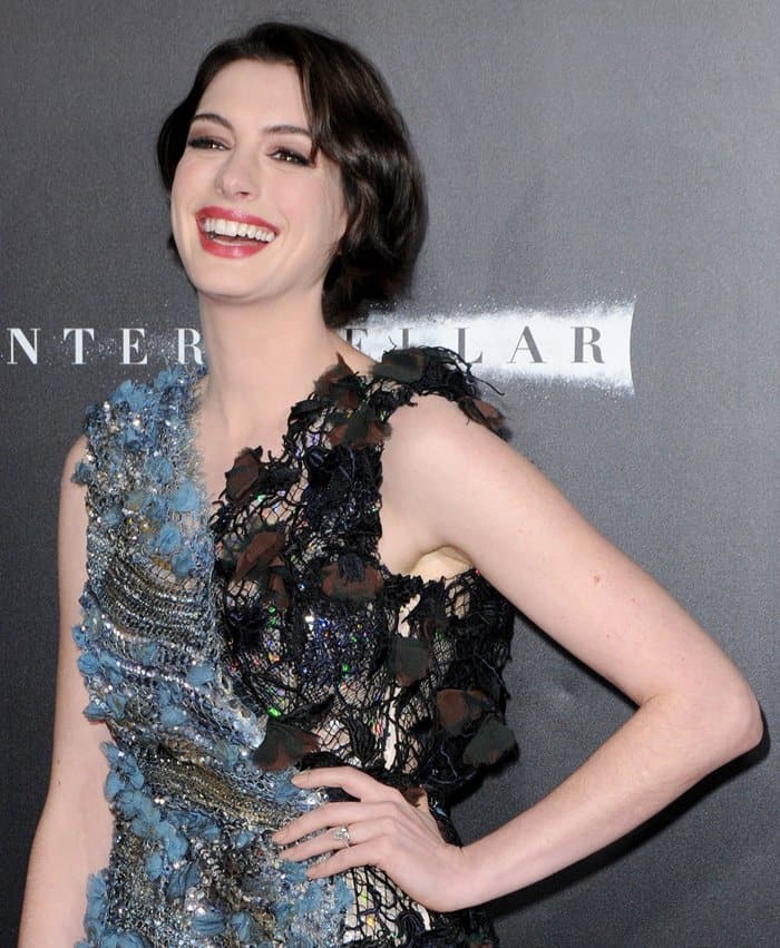Anne Hathaway radiates elegance with her wavy bob hairstyle and a bold rouge lip, perfectly complementing her intricate Rodarte dress