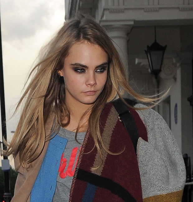 Cara Delevingne is seen wearing a Burberry Prorsum color-block check blanket poncho and a casual gray top, her makeup featuring smoky eyes and her hair styled naturally