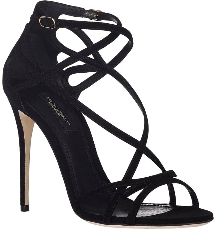 Dolce Gabbana's black suede sandals feature slender crisscross straps, an elegant ankle strap with a gold-tone buckle, sculpted heel counters, and towering stiletto heels, creating a timeless silhouette that balances minimalist sophistication with striking red-carpet appeal