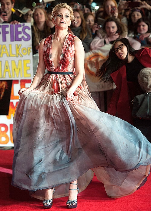 Elizabeth Banks adjusting the skirt of her gown and showing her shoes from underneath the hemline