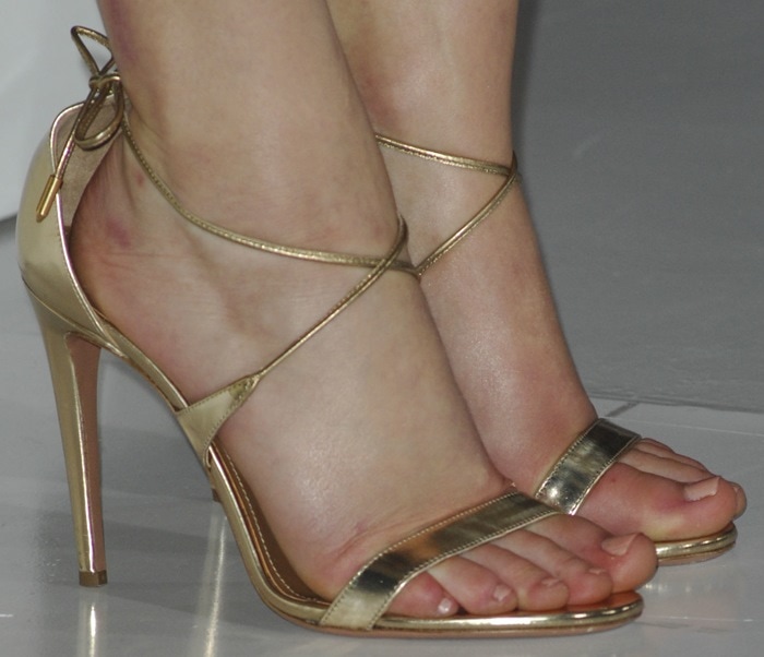 A closer look at Jennifer Lawrence’s gold-tone Aquazzura “Linda” sandals, featuring delicate wraparound ankle straps and a sleek stiletto heel that elongates the leg without overpowering the dress