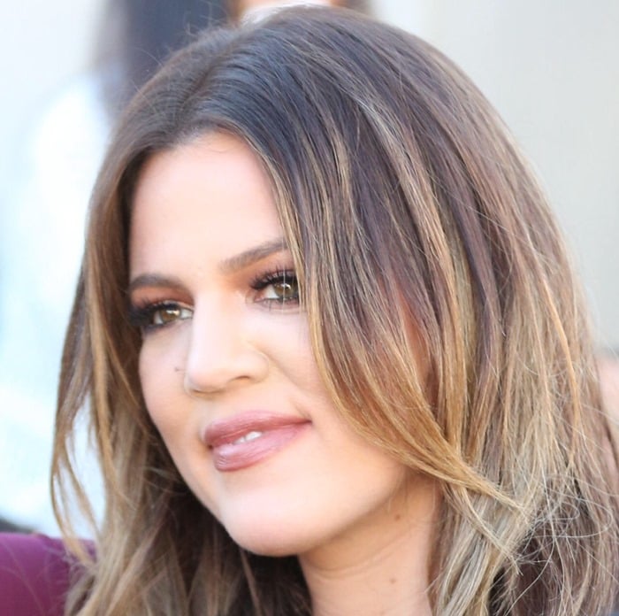 Khloé Kardashian showcases her signature beauty look with voluminous, loose waves, glossy nude lips, and defined eye makeup that enhances her hazel eyes