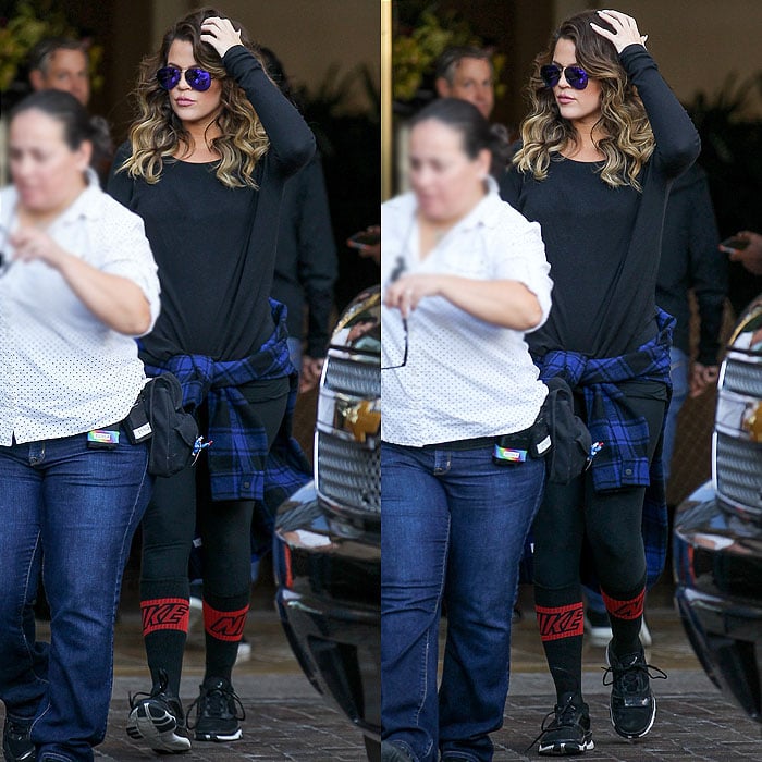 Khloé Kardashian swaps her white co-ord for a laid-back, sporty outfit featuring black leggings, red Nike socks, and a plaid shirt tied around her waist