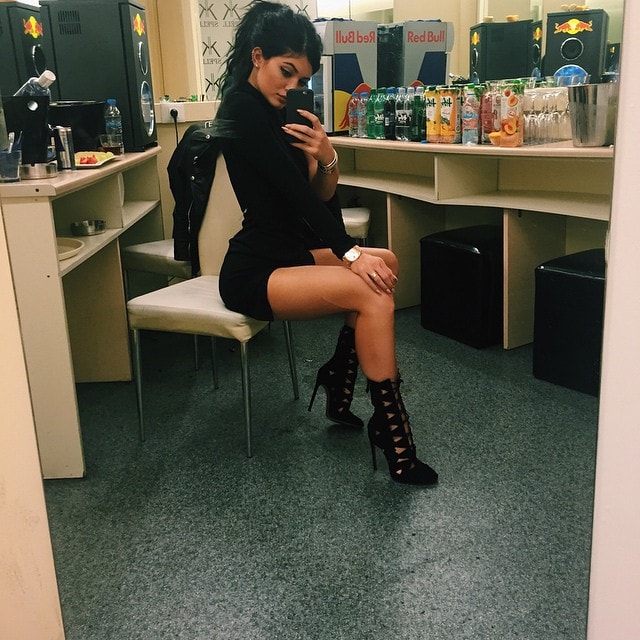 Kylie Jenner strikes a mirror selfie pose in a sleek black mini dress paired with Alaïa’s cut-out suede lace-up ankle boots