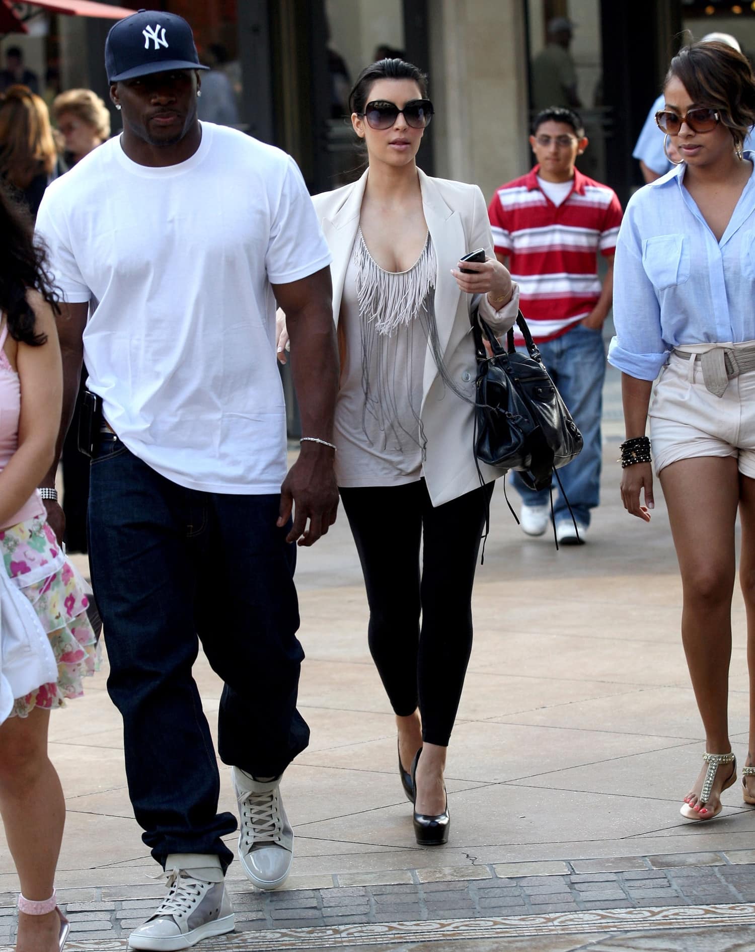 Kim Kardashian steps out in black metallic platform pumps with a cream blazer, fringe top, and leggings alongside Reggie Bush in high-top sneakers and La La Anthony during a shopping trip
