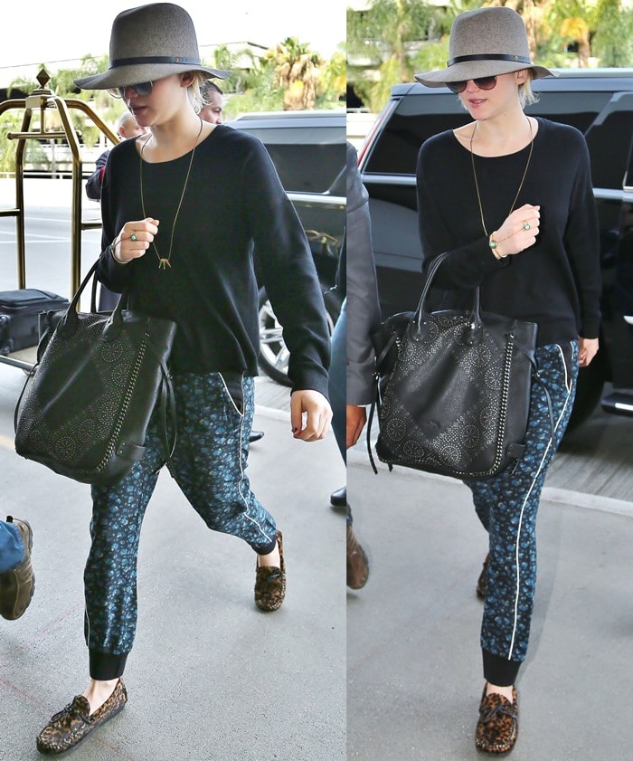 Hunger Games star Jennifer Lawrence wearing a wide-brimmed hat, oversized sunglasses, loose-fitting tapered black trousers with a blue floral design, and leopard-print moccasins at Los Angeles International Airport (LAX)