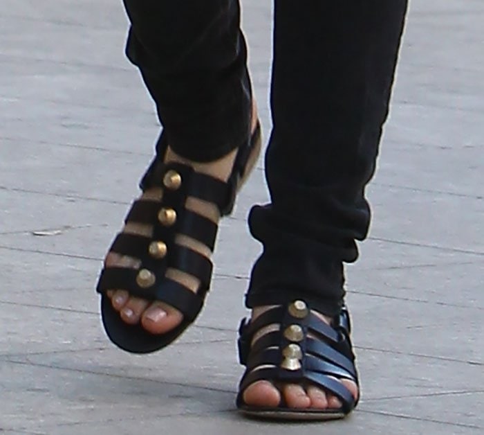 Kaley Cuoco shows off her feet in flat black Balenciaga leather sandals, featuring wide caged straps and bold gold dome studs for a luxe, edgy finish
