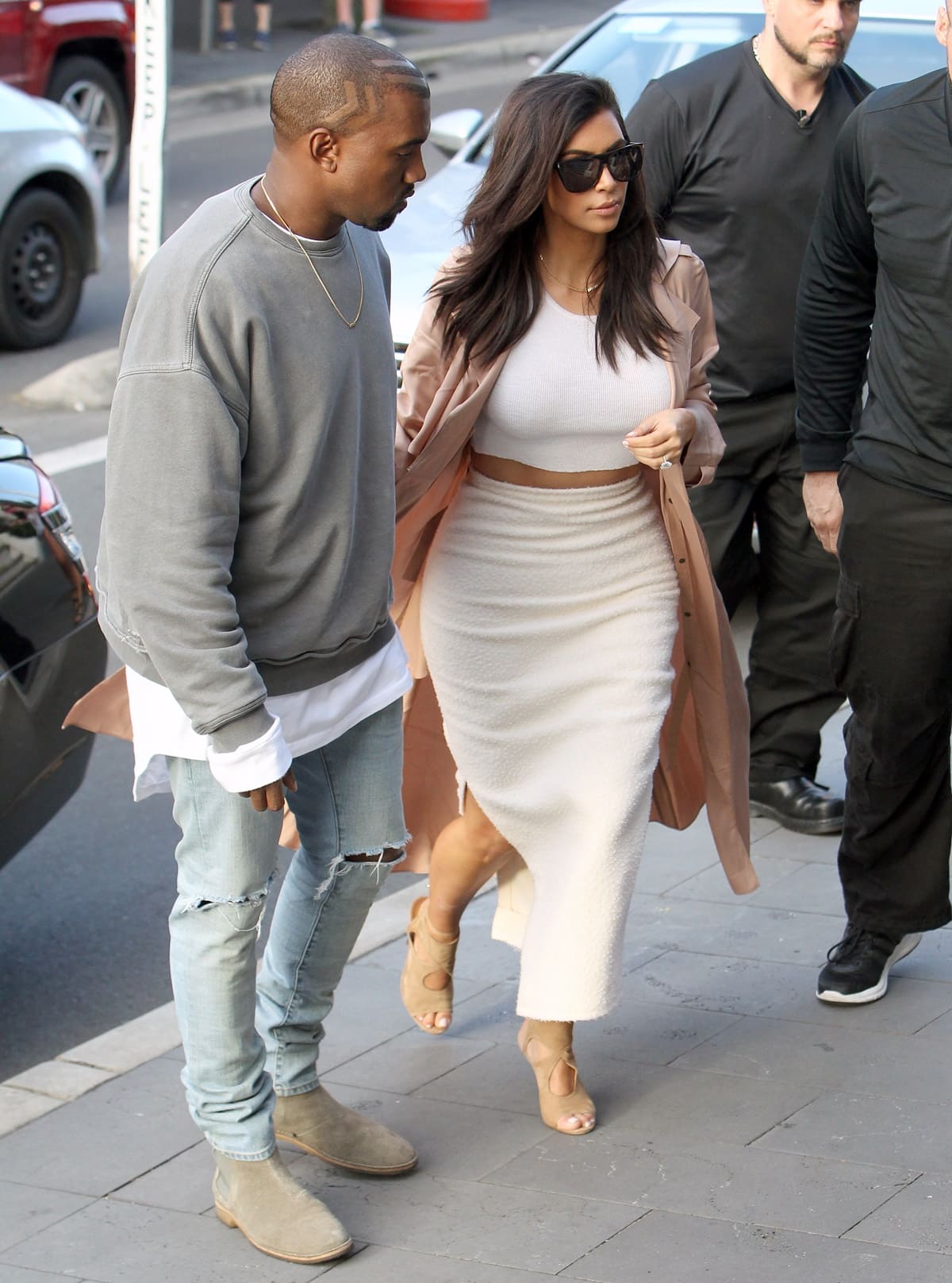 Kim Kardashian steps out in Aquazzura's “Sexy Thing” sandals paired with a cropped white top, fitted midi skirt, and blush trench coat during a lunch date with Kanye West in Sydney, Australia, on September 14, 2014