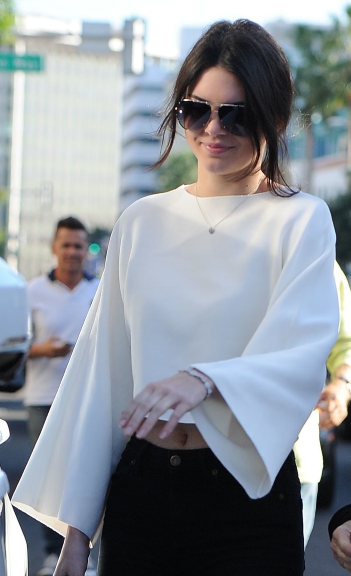 Kendall Jenner wearing a white flared-sleeve crop top, black skinny jeans, and Saint Laurent python ankle boots in Beverly Hills