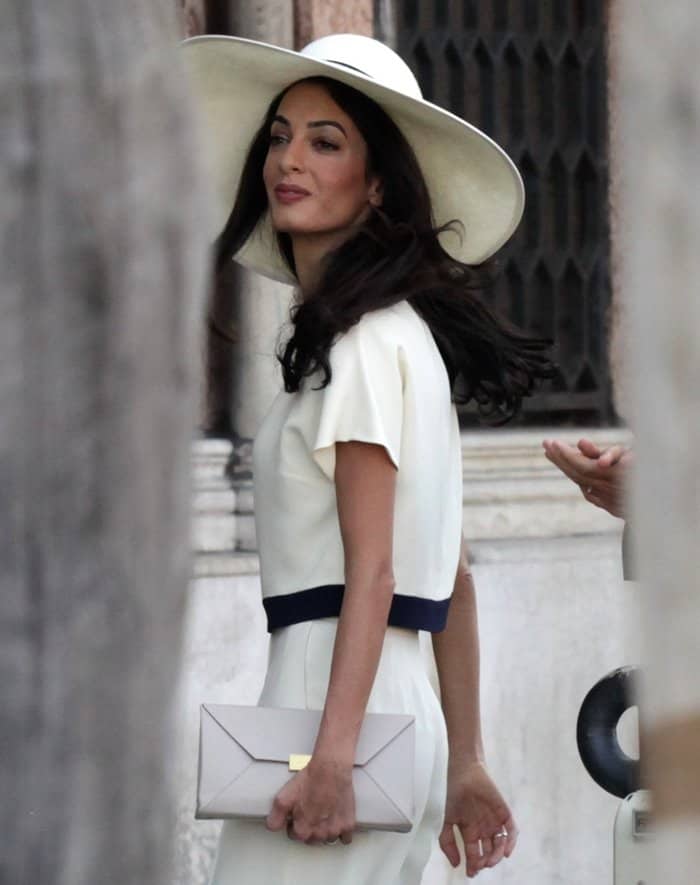 Amal Alamuddin stuns in a sleek ivory two-piece suit, cinched with a navy band and paired with a structured Stella McCartney clutch during her wedding weekend in Venice