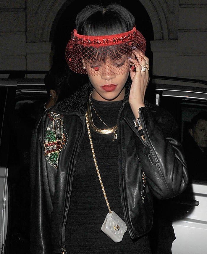 Rihanna exudes edgy elegance with a red netted visor, gold layered necklaces, and a super tiny Chanel purse slung crossbody over her embellished leather jacket