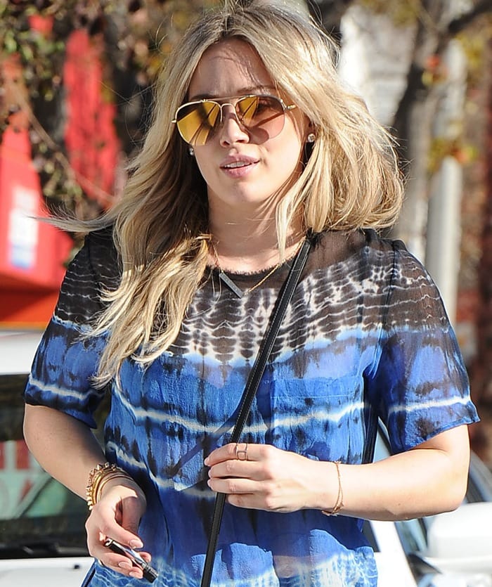 Hilary Duff steps out in a breezy tie-dye top, accessorized with mirrored aviator sunglasses and delicate gold jewelry for an effortlessly chic daytime look