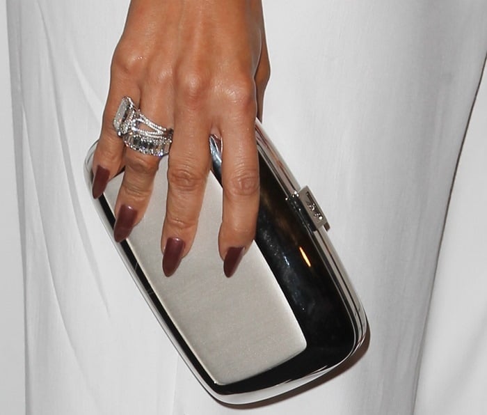 Jennifer Lopez accessorizes her monochromatic look with a sleek metallic clutch and stacked diamond rings, complementing the sharp elegance of her all-white ensemble