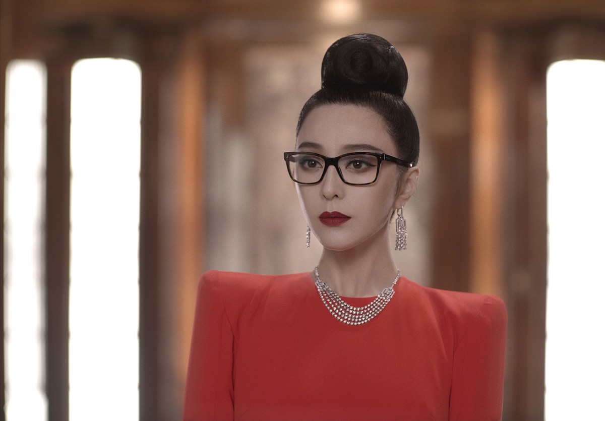 Fan Bingbing exudes sophistication and mystery in The 355, wearing a striking red dress, statement jewelry, and sleek glasses, embodying a poised yet enigmatic presence