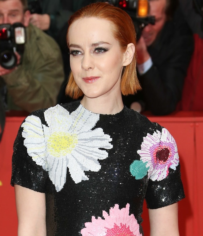 Jena Malone turned heads in a shimmering black sequin Thom Browne dress adorned with oversized floral embellishments, complemented by sleek, slicked-back copper hair and minimal accessories to let the bold print shine