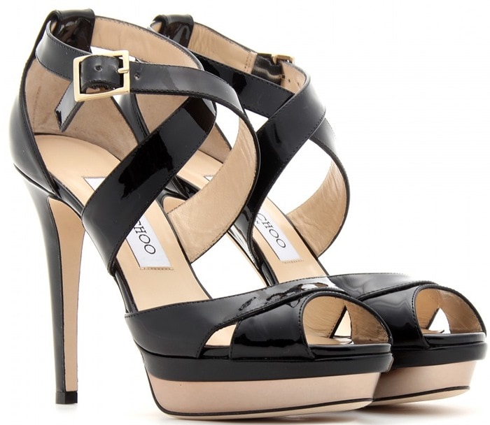 Black patent Jimmy Choo Kuki platform sandals feature glossy crisscross straps, a secure buckle-fastening ankle strap, a subtle front platform, and a slender covered stiletto heel that balances height with stability for formal occasions