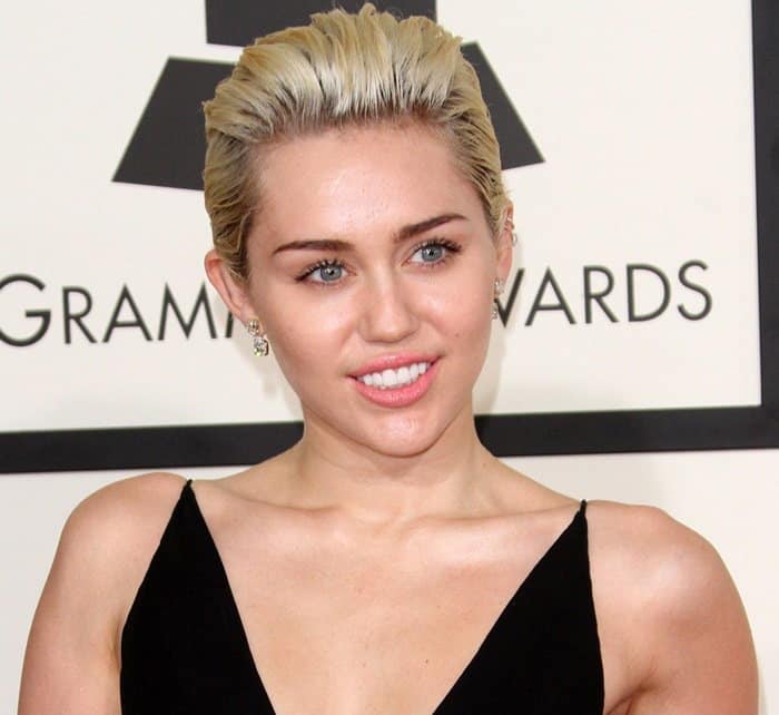 Miley Cyrus rocking a slicked-back platinum blonde hairstyle paired with delicate diamond stud earrings for a sophisticated touch